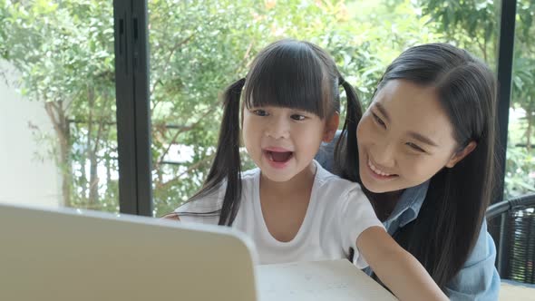 Young asian mother shows her daughter a cartoon or movie from her laptop.
