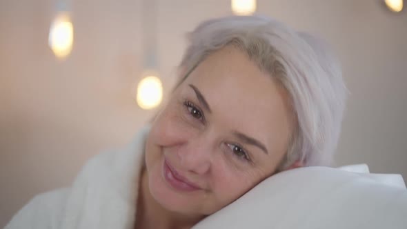 Closeup Front View Positive Mature Woman Smelling Fresh Clean Laundry Smiling Looking at Camera alt