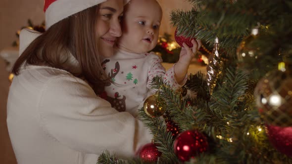 Baby in Mom Arms on Christmas Night By the Tree