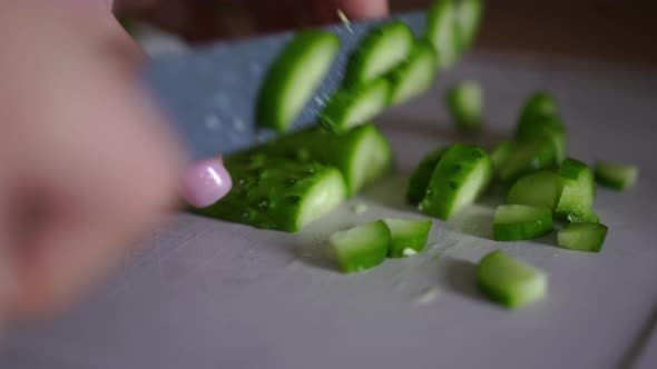 Woman Cuts Cucumber with Knife on Board at Home in Kitchen