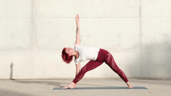 Woman doing warrior two yoga into extended triangle pose on street alt