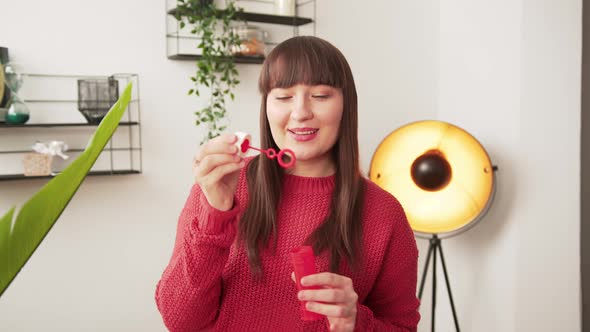 Young Caucasian Brownhaired Woman Playing with a Soap Bubble Blowing Toy Indoors alt