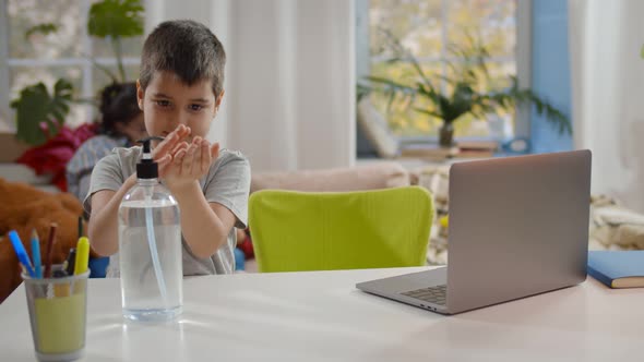 Little Boy Applying Hand Sanitizer Gel While Studying with Laptop at Home alt