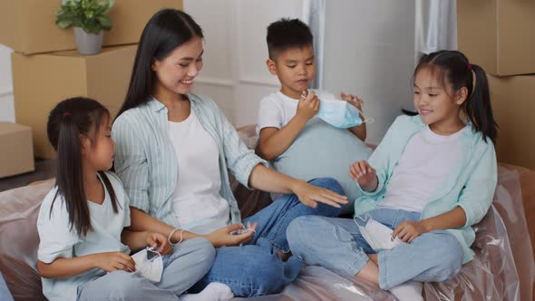 Asian Family Taking Off Masks Sitting Among Moving Boxes Indoor alt
