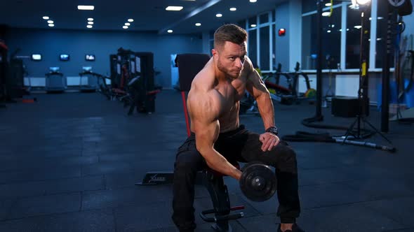 Power fitness man biceps. Handsome sportsman exercising with dumbbell while sitting in gym alt
