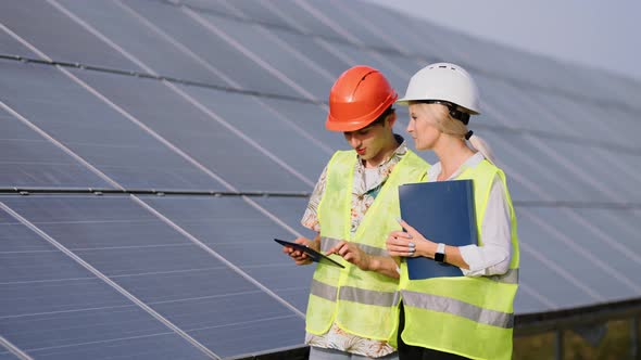 Beautiful Female Engineer and Young Male Trainee They are Standing at a Solar Panel Station