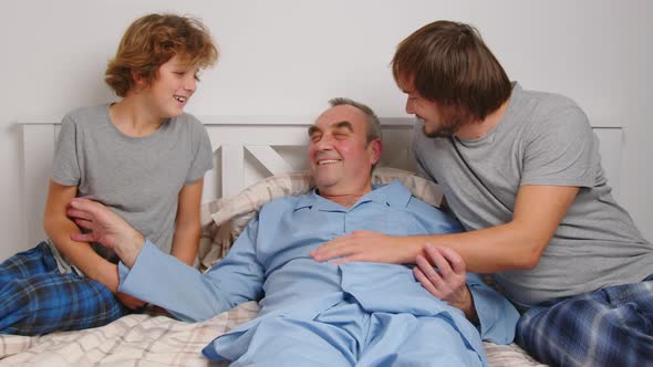 Aged Male Patient Embracing Kids and Talking While Lying on Bed at Home alt