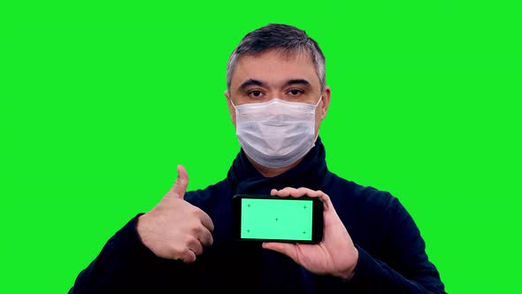 Portrait of Asian Man in Protective Mask Showing Smartphone with Green Screen and Thumb up