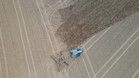 Top down over farm field being tilled for autumn. Blue tractor working hard.