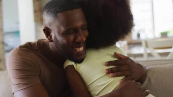 African american daughter and her father smiling and hugging on couch alt