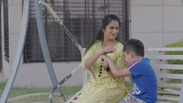 Indian Mother with her cute son playing together on garden swing making face expressions