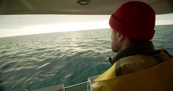 Sailor Looks Over the Side of the Boat Into the Water at Sunset