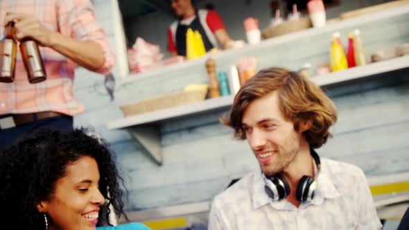 Group of friends toasting beer bottle while having meal alt