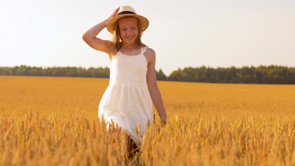 happy girl in straw hat walking along cereal field alt