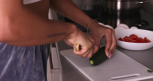 Black woman with knife cuts the cucumber.
