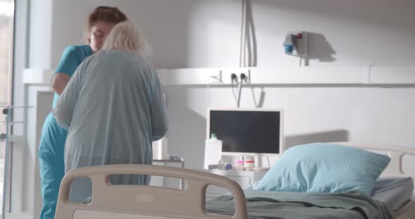 Young Nurse Supporting Senior Female Patient Walking to Bed in Hospital alt
