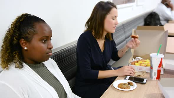 African American woman laughs at joke while eating lunch with Caucasian friend alt