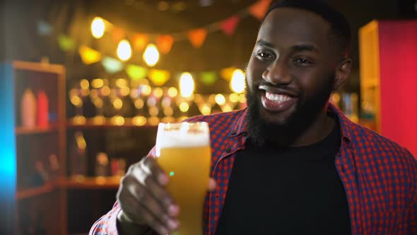 Cheerful African-American Male Clinking Beer Glass, Enjoying Results Time in Bar alt
