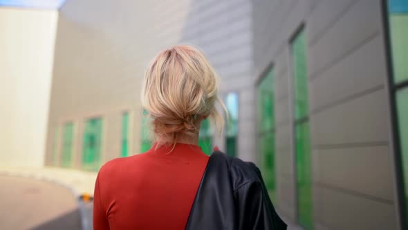 a Blonde in a Red Dress with a Black Jacket Over Her Shoulder Walks Along the Wall with Large alt