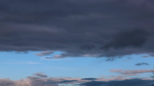 Time-lapse video of fast moving dark clouds against strip of blue sky in late afternoon alt