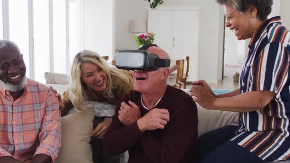 Two diverse senior couples sitting on a couch caucasian man is using vr googles alt