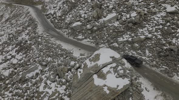 Aerial shot of car in the street with snow caped mountain in the side. alt
