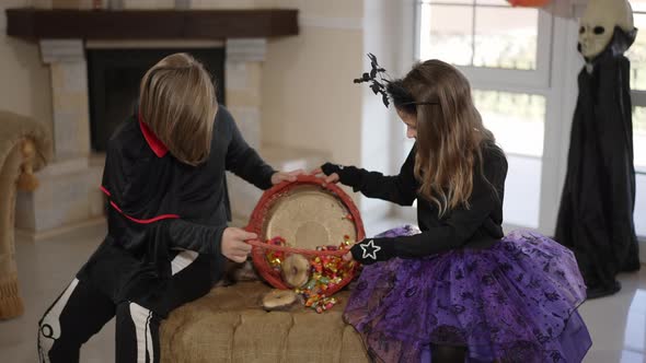 Happy Boy and Girl with Trick or Treat Basket of Candies Sitting Indoors Examining Sweets alt