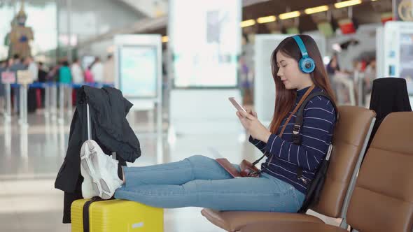 Young female traveler listening music from headphone at airport alt