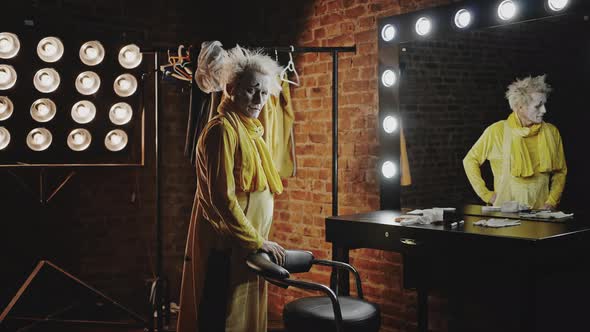Sad Mature Actor in Yellow Costume Stands in Dressing Room alt