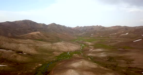 Fresh brown hills and green meadow with small rivers in highlands with mountain landscape in backgro alt