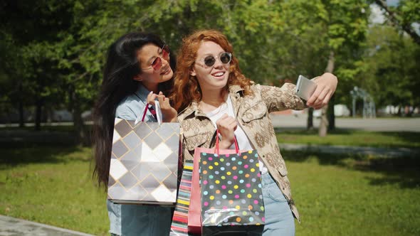 Pretty Girls Taking Selfie with Smartphone Holding Shopping Bags in City Park alt