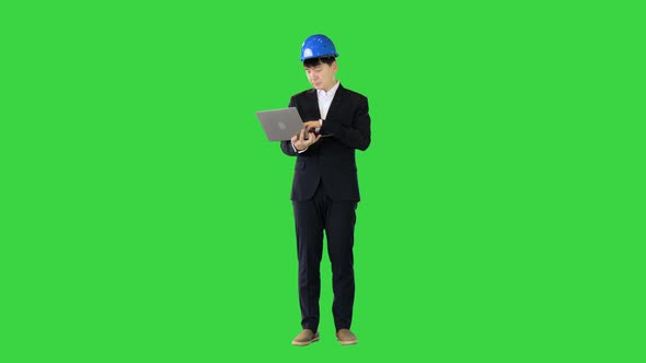Engineer in a Suit Standing and Working on a Laptop on a Green Screen Chroma Key alt