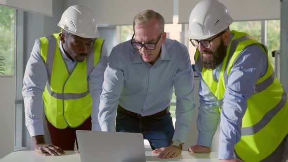Architects Discussing Blueprint on Laptop with Construction Manager in Office alt