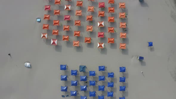 Aerial top down view of a beach filled with beach tents in red and blue  alt