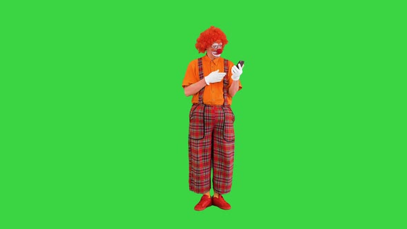 Funny Clown Looking at Smartphone and Reacting on What He Sees on a Green Screen Chroma Key alt