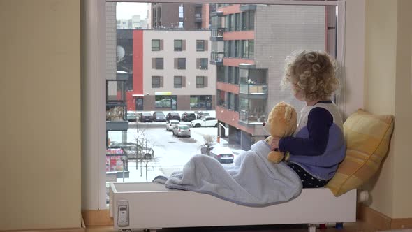 Girl with Best Friend Teddy Bear Looking at Snow Fall Blizzard through Window