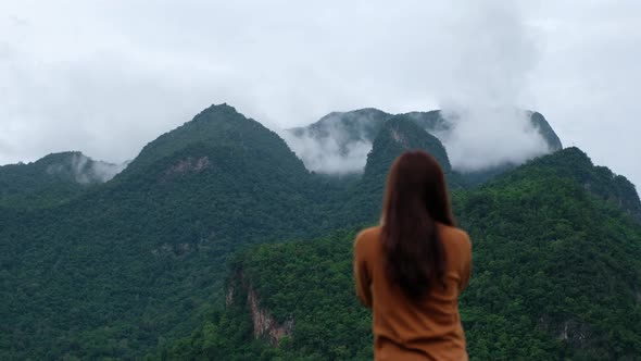 A female traveler taking a photo of a beautiful greenery mountains on foggy day