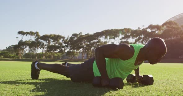 Fit african american man exercising outdoors doing press ups holding dumbbells alt