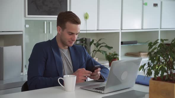 Young Businessman in the Modern Office Using App on Smartphone. alt