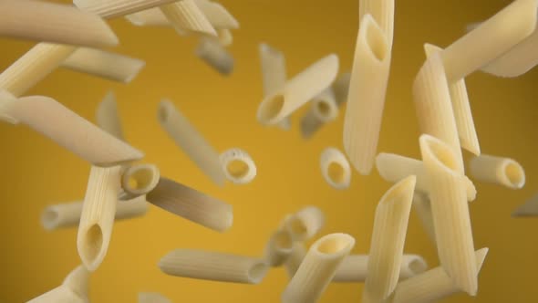 Dry Raw Pasta Penne Bouncing and Rotating on a Yellow Background alt