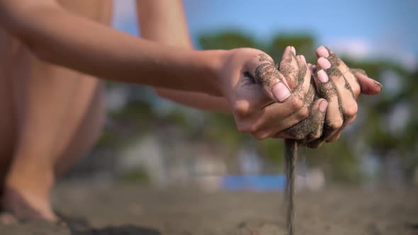 close-up hand grabs a handful of dry sand and lets it fall between his fingers alt