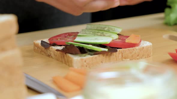 Woman's hands put fresh carrots slice on healthy sandwich, Close up.