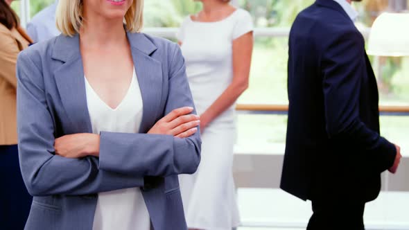 Female business executive smiling at camera while colleagues interacting in background alt