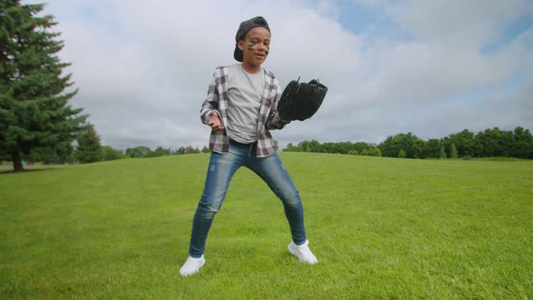 Joyful School Age African Boy with Baseball Glove and Ball Dancing on Field alt
