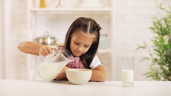 Child Pours Milk Into a Bowl of Cereal in the Kitchen.