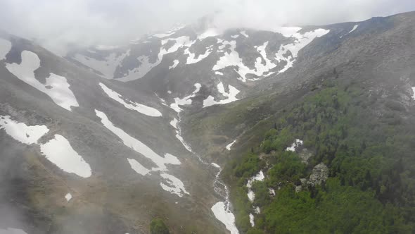 Aerial Forested Mountain With Snow Fragments Among The Clouds in The Spring alt