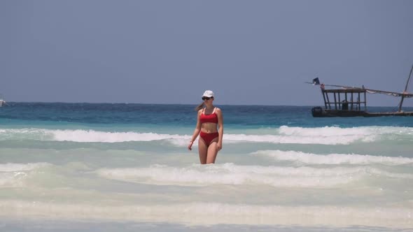 Young Woman in a Red Swimsuit Walks Into the Turquoise Ocean on a Paradise Beach alt