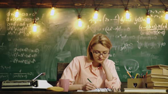 Teacher Woman Sitting in the Classroom While Reading and Write on the Book. Student Studying Near alt
