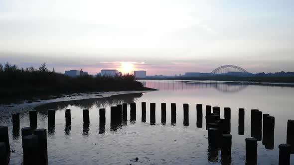 Silhouetted Wooden Poles in Water and Trees on the River Bank, Revealing Spectacular City with Arch alt