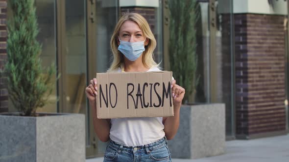Young White Woman a Medical Mask Holding Carton Poster with Writing Slogan No Racism. Concept of the alt